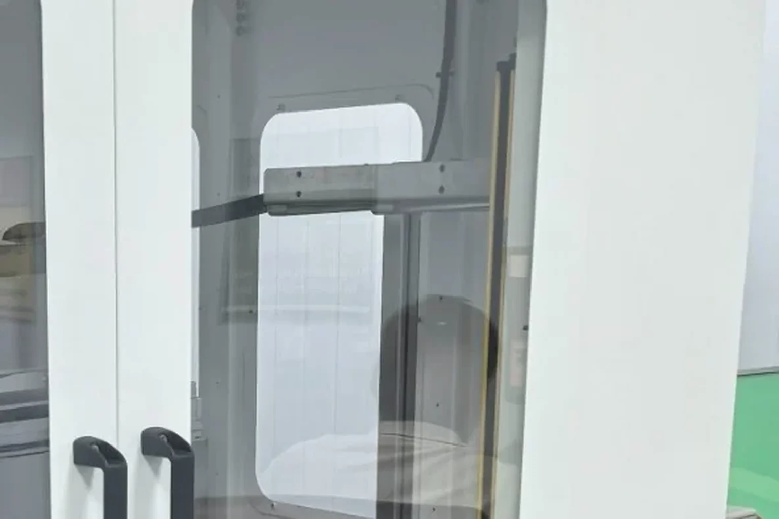Two glazed doors of a white machine enclosure, seen from the front on a green epoxy floor