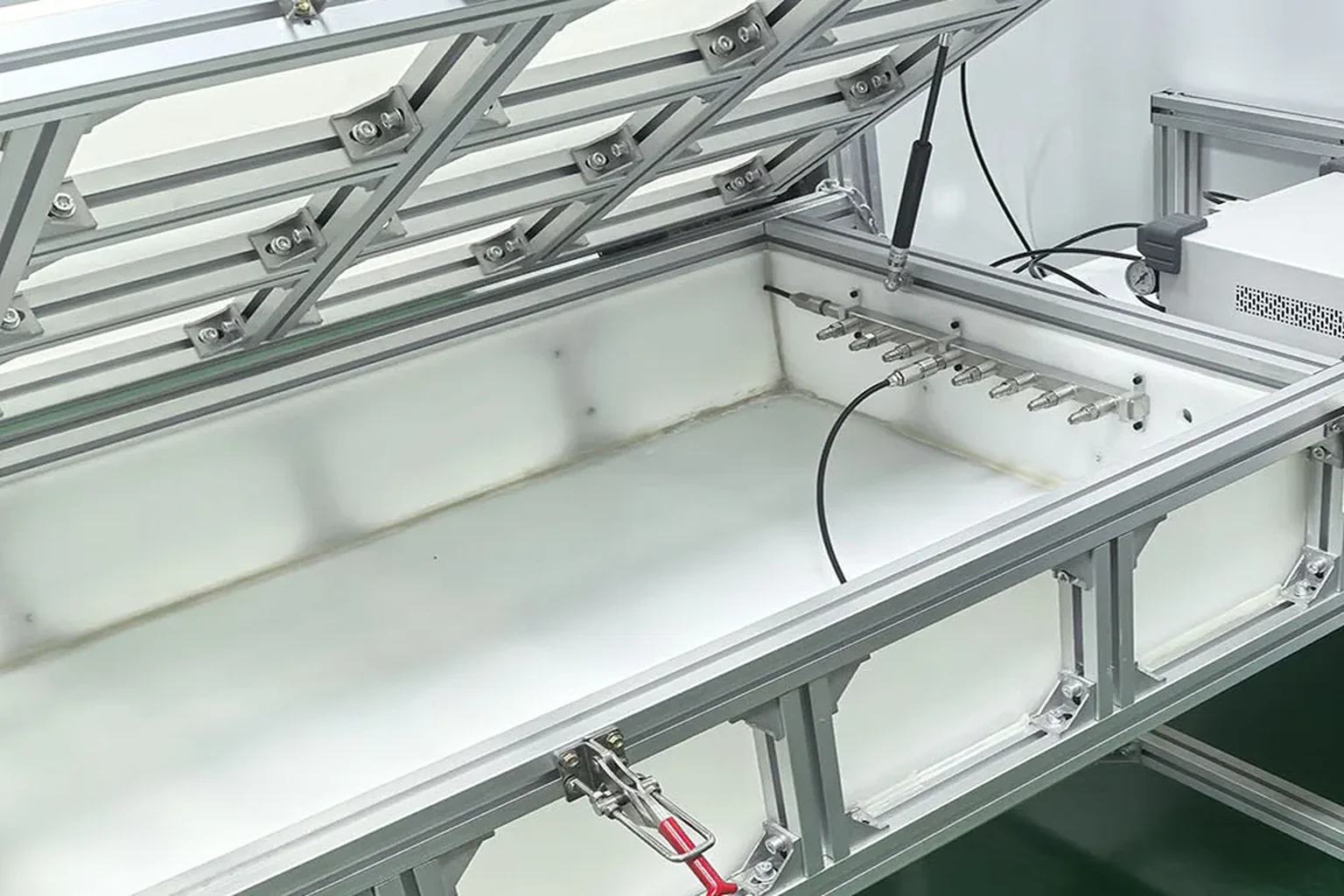 A white-lined tank set into an aluminium frame, with a row of quick-connect fittings across it and the lid propped open